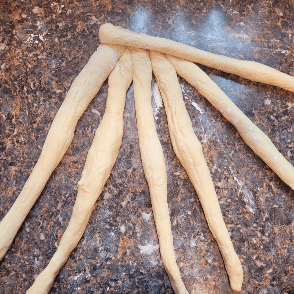 Image illustrates dough for a 6 braided challah bread recipe demonstrating how to braid a challah bread.