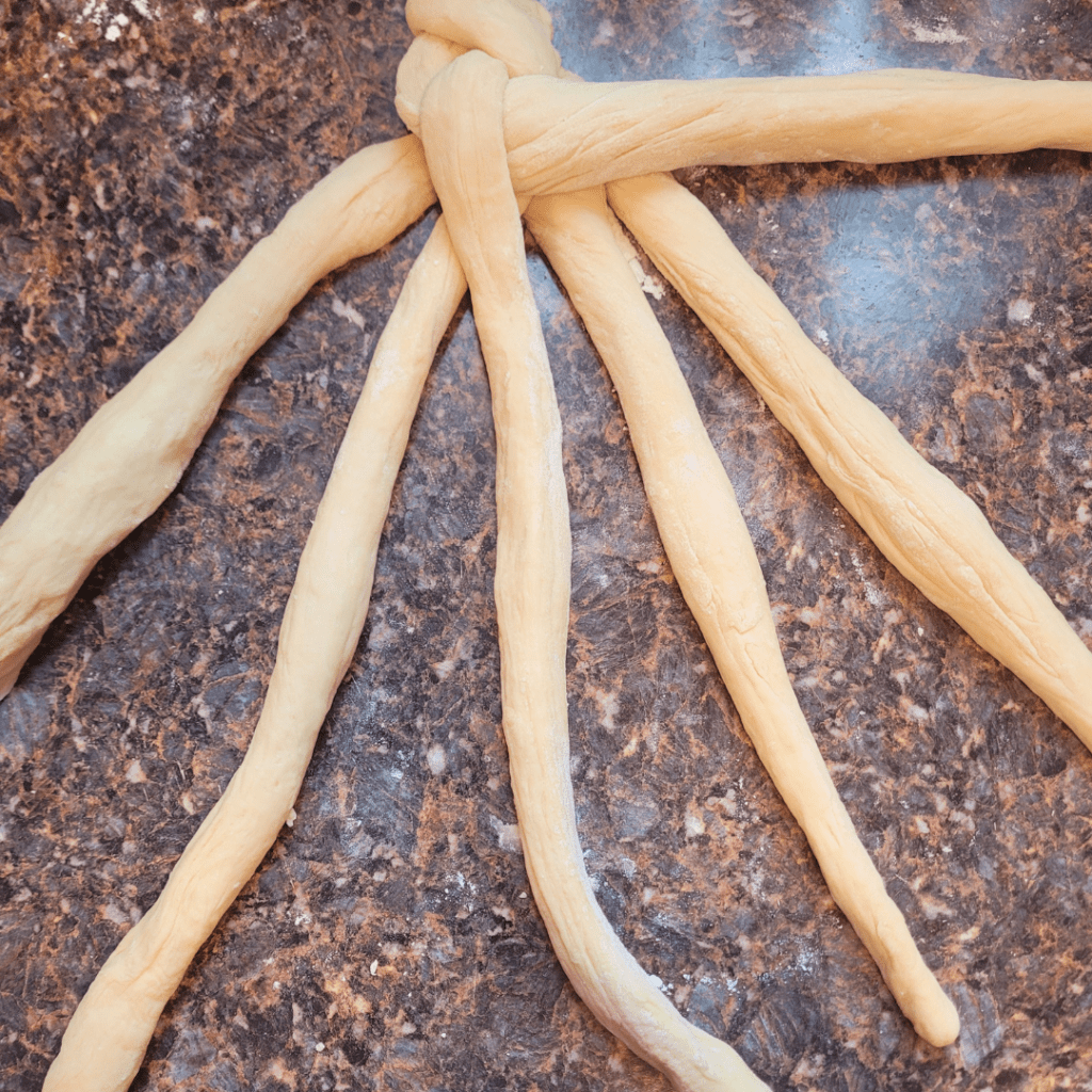 Image illustrates dough for a 6 braided challah bread recipe demonstrating how to braid a challah bread.