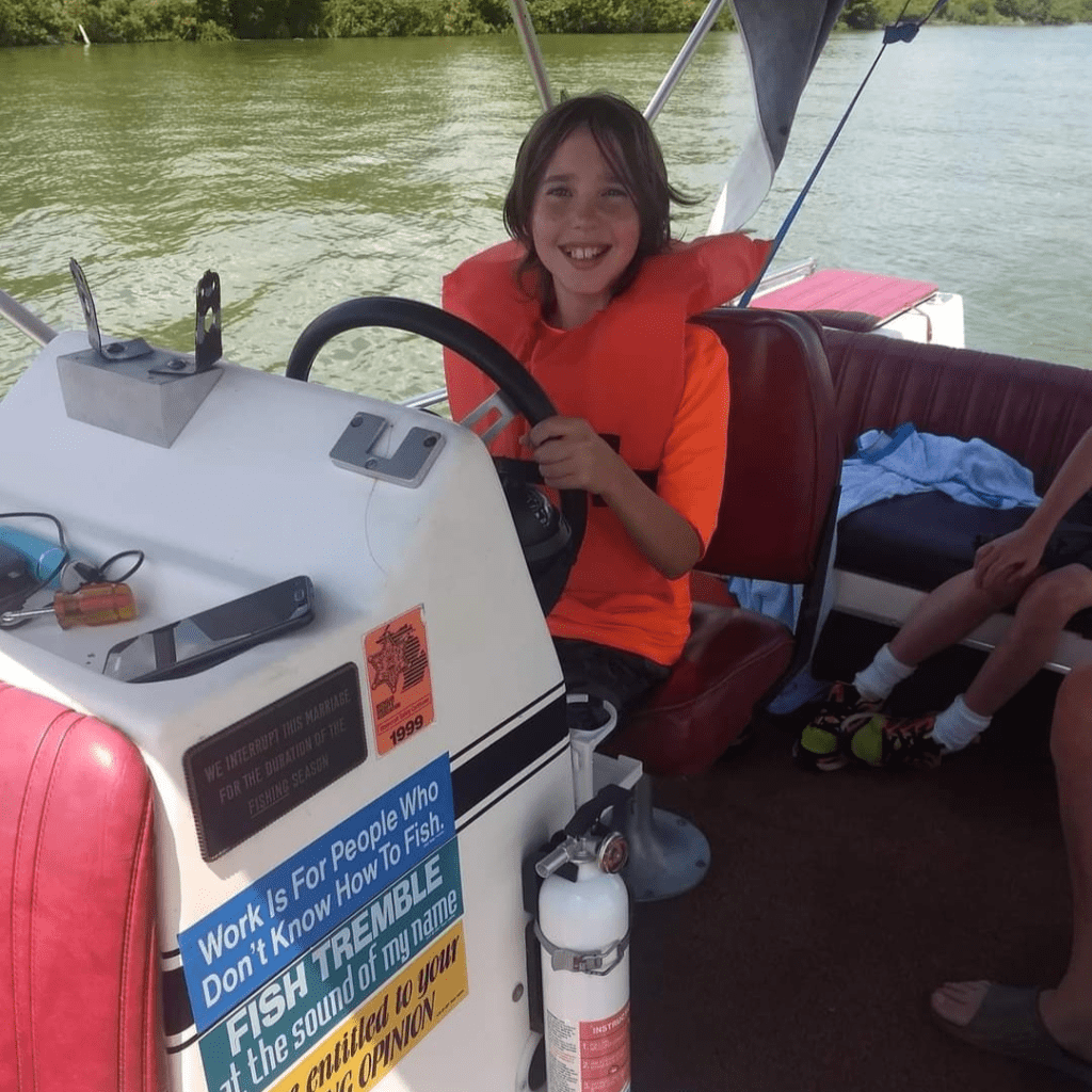 Image illustrates an image of a kid driving a boat for lake fishing with kids.