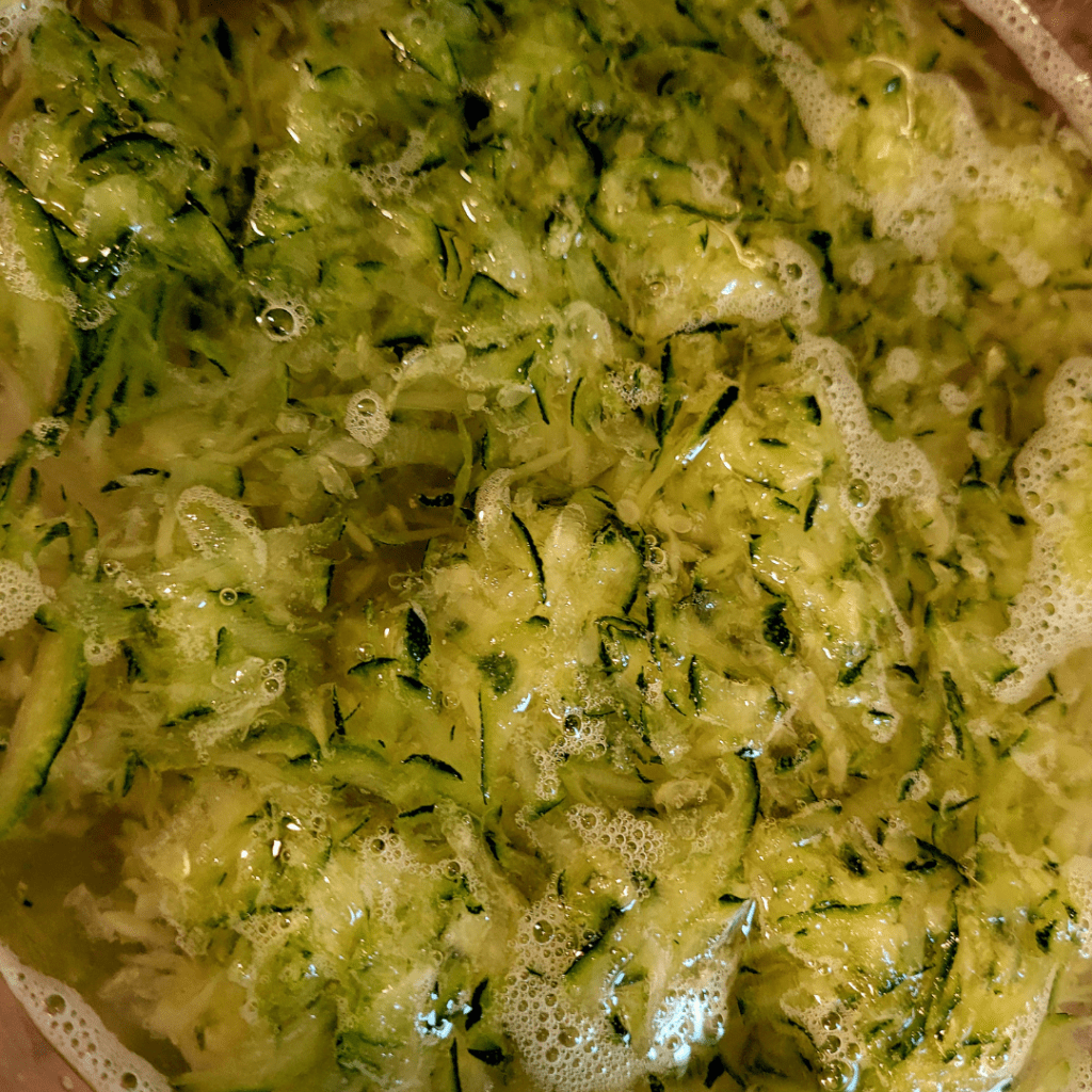 Image illustrates shredded zucchini soaking in salt water to balance out the bitter taste caused by environmental elements causing high amounts of cucurbitacin levels for making snickerdoodle zucchini bread. 