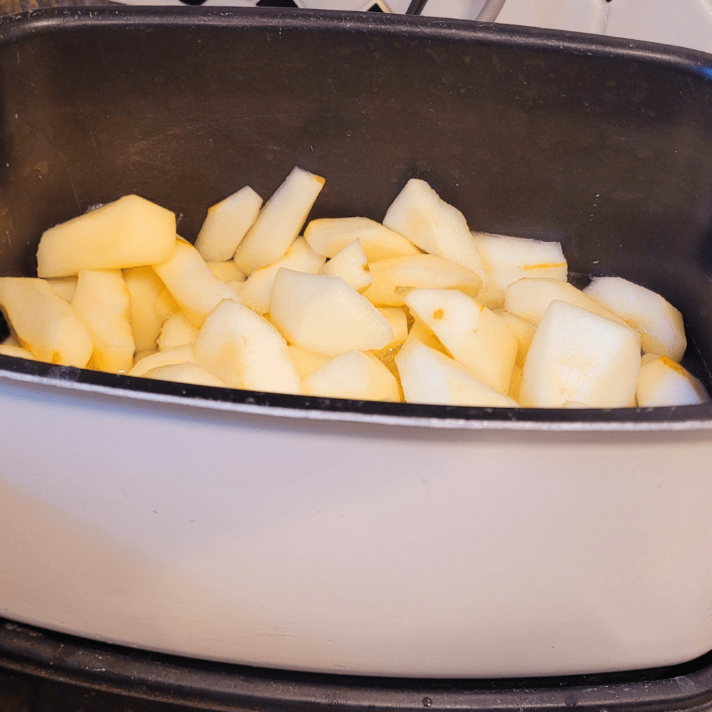 Image illustrates chopped pears in a slow cooker cooking down for canning pear sauce.