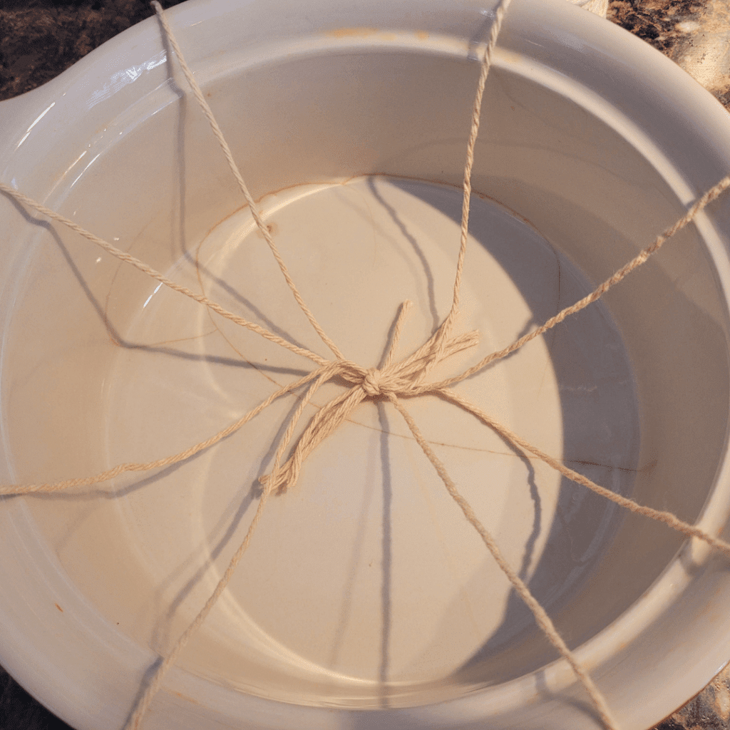 Image illustrates a small Dutch oven with cotton string ready for proofing pumpkin-shaped sourdough bread. 