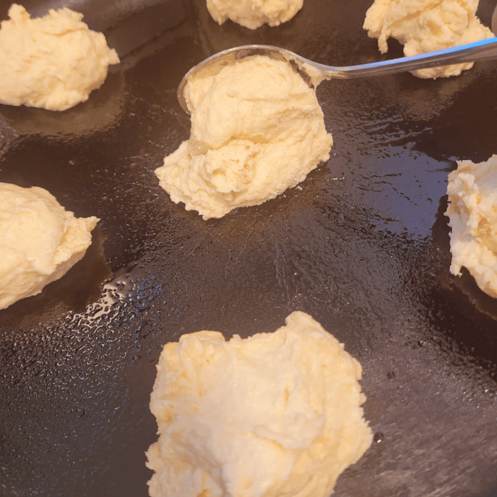 Image illustrates sourdough buttermilk drop biscuits on a cast iron baking pan.