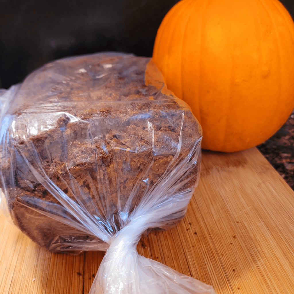 Image illustrates wrapped pumpkin bread with a pumpkin for a pumpkin bread recipe.