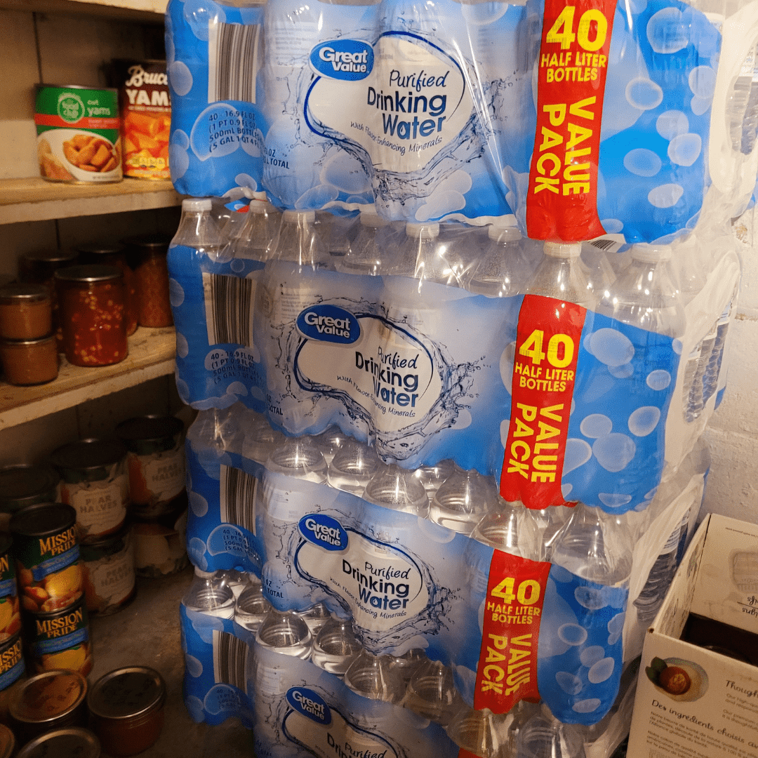 Image illustrates a stack of bottled water and pantry food demonstrating how to stock a working pantry.