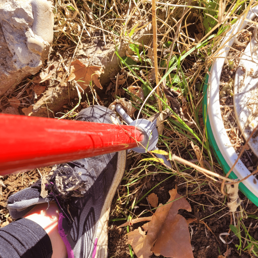 Image illustrates a foot pushing down on a garden hand tiller into the soil demonstrating how to use the hand twist garden tiller.