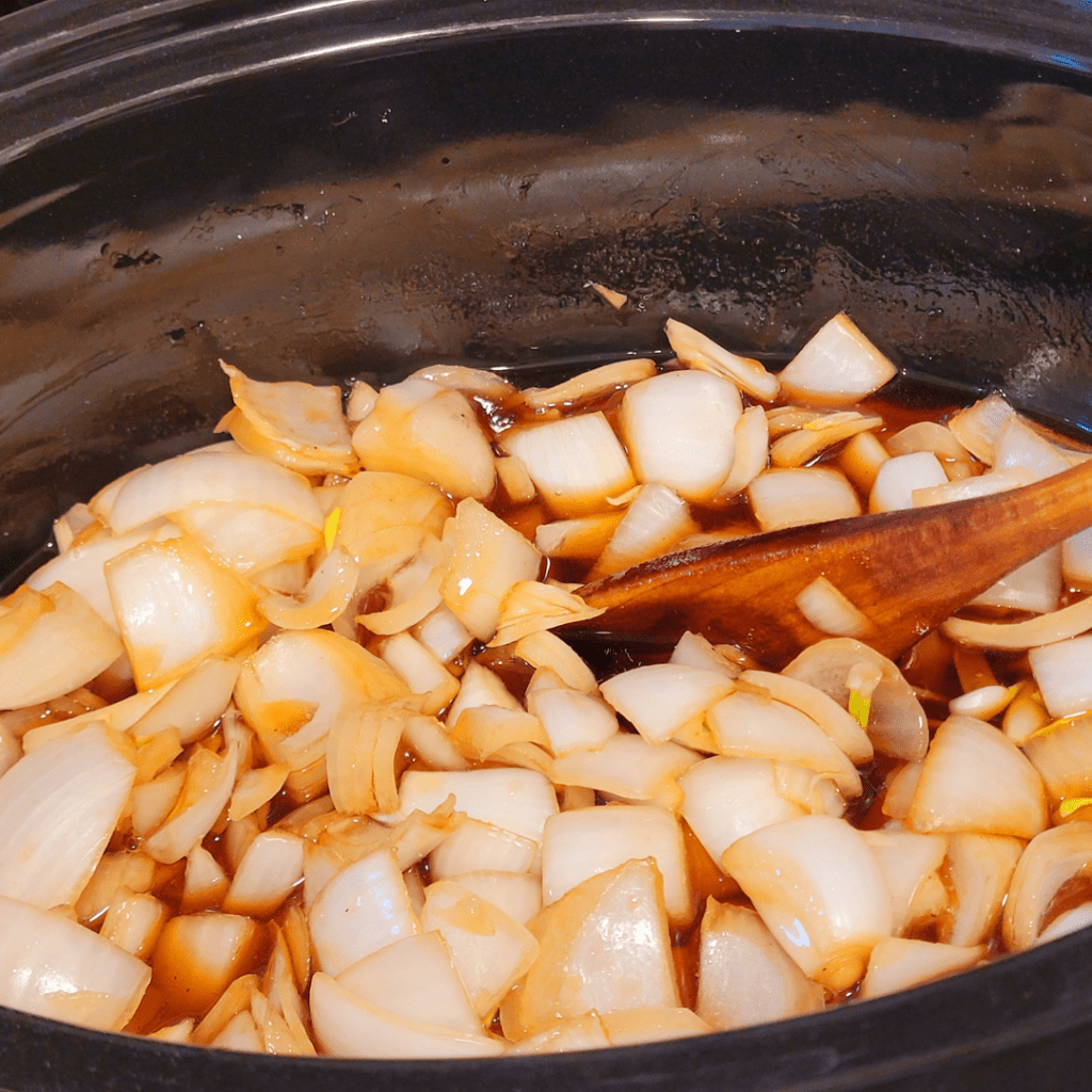 Image illustrates onions being cooked in a crockpot for a balsamic onion jam recipe.