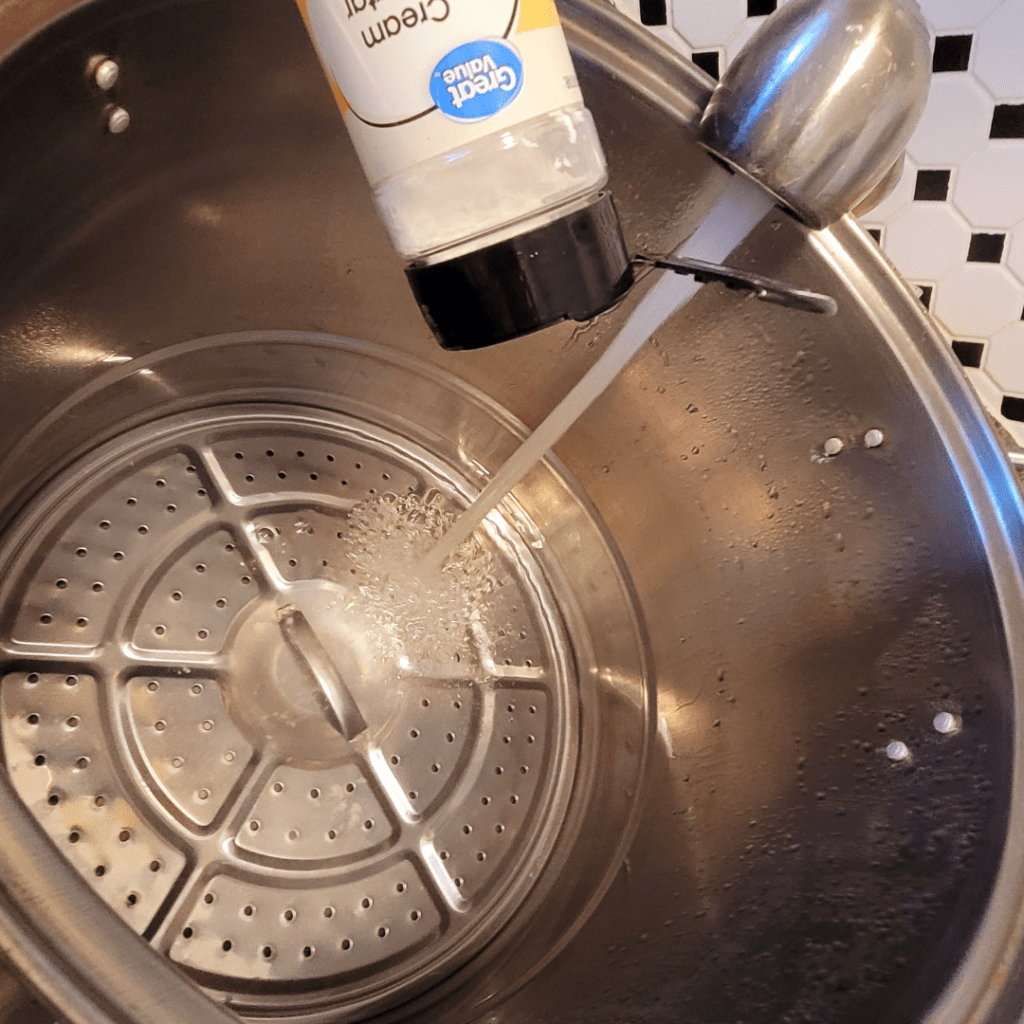 Image illustrates a water bath canner being prepared for canning with cream of tarter to prevent rust on the rings.