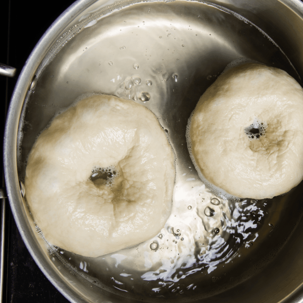 Image illustrates bagels being boiled before baking. 