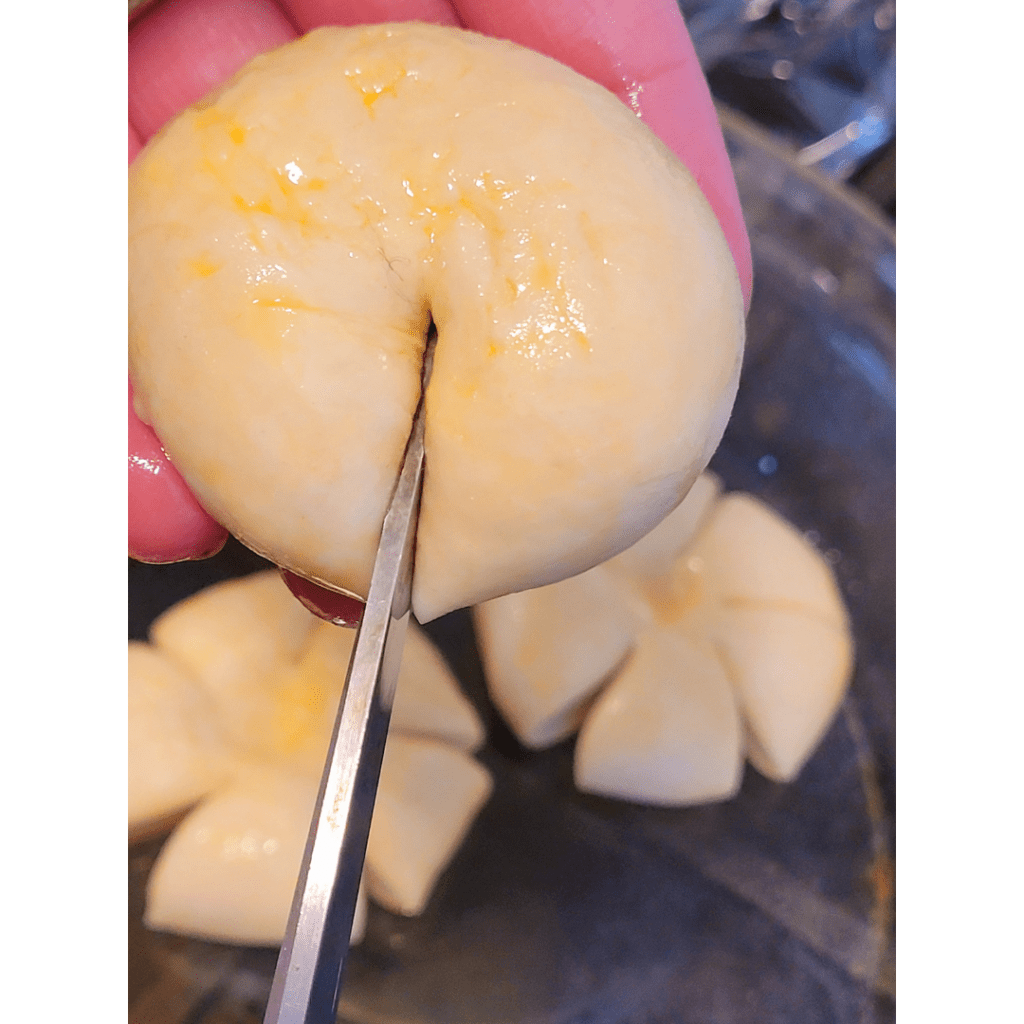 Image illustrates a dough ball being cut with scissors to create pumpkin-shaped bread rolls. 