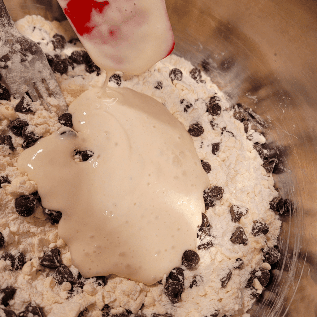 Image illustrates sourdough discard being added into a mixture for sourdough discard scones. 