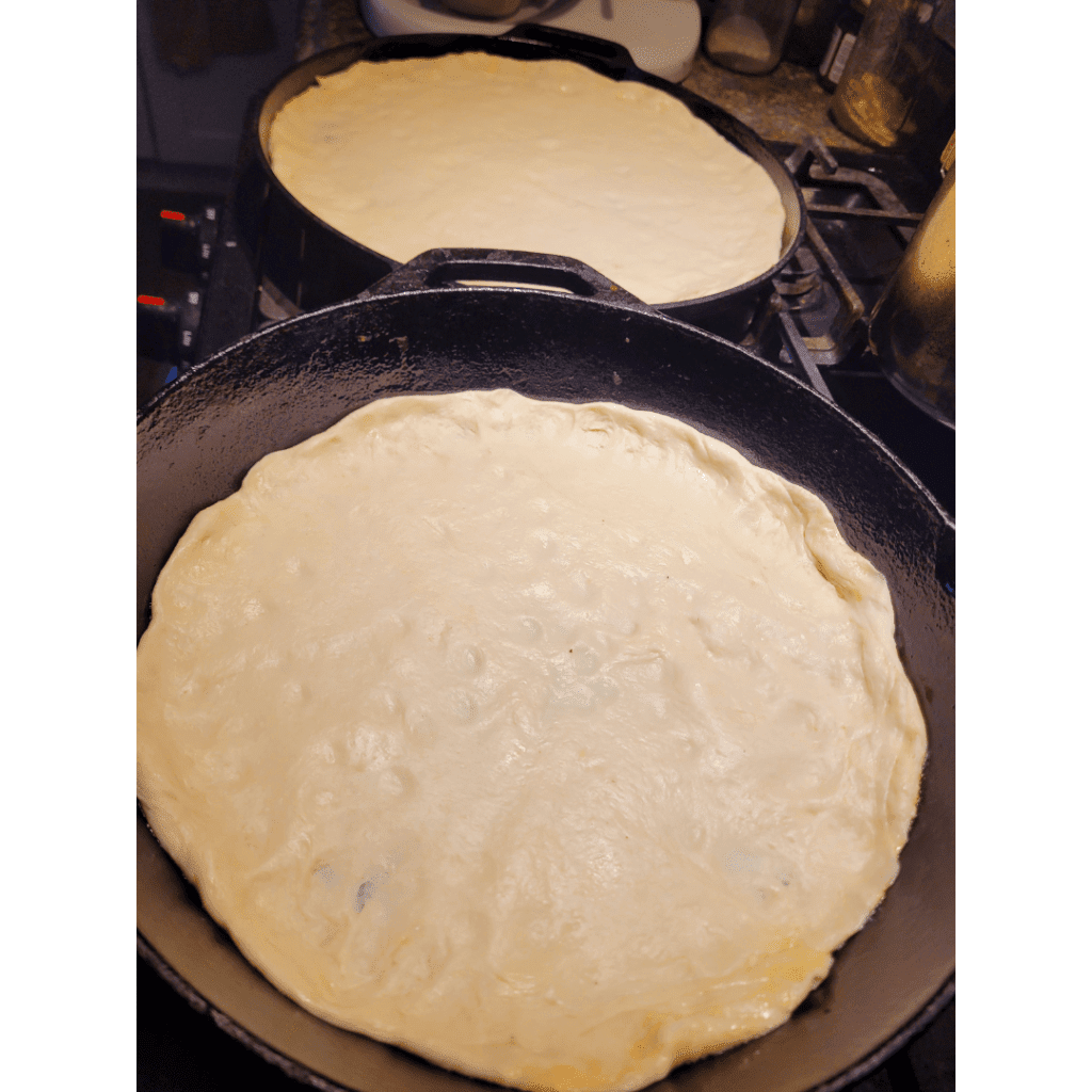 Image illustrates sourdough pizza dough rolled out on cast iron pans. 