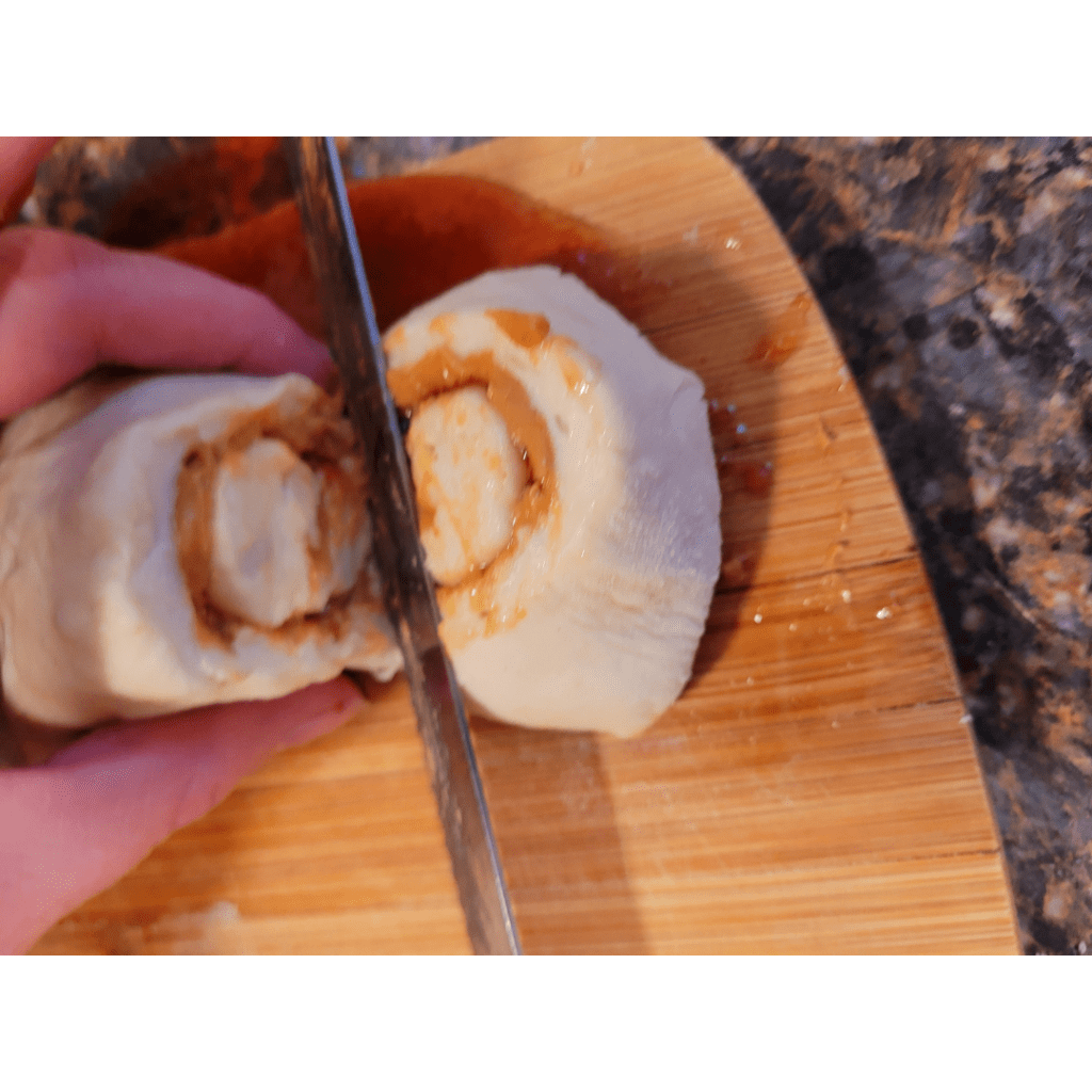 Image illustrates a person slicing rolls from a dough log.