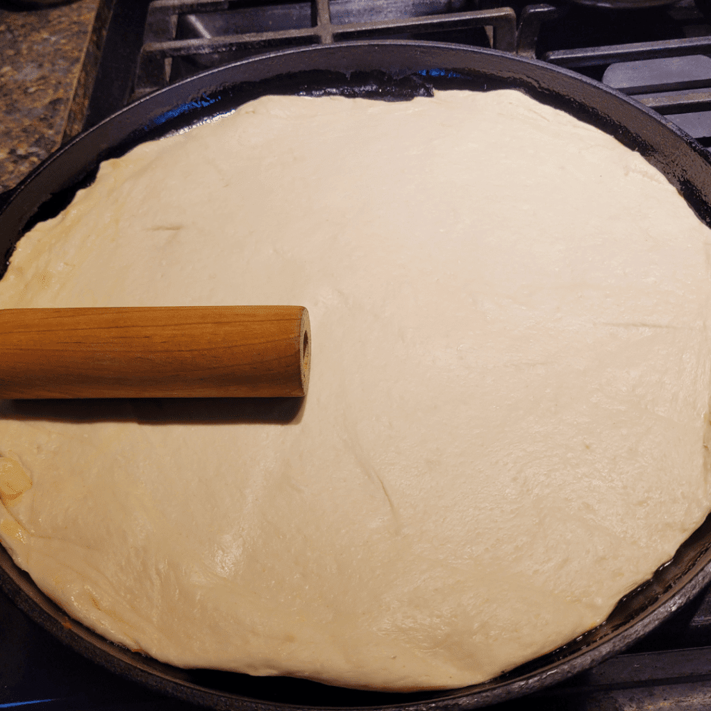 Image illustrates sourdough pizza dough rolled out on a cast iron pan. 