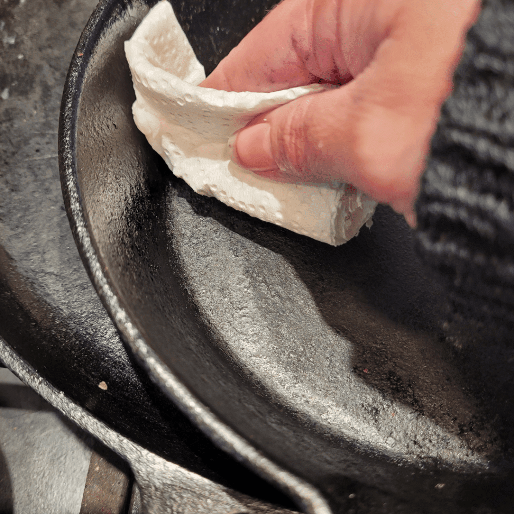 Image illustrates a person seasoning a cast iron pan. 