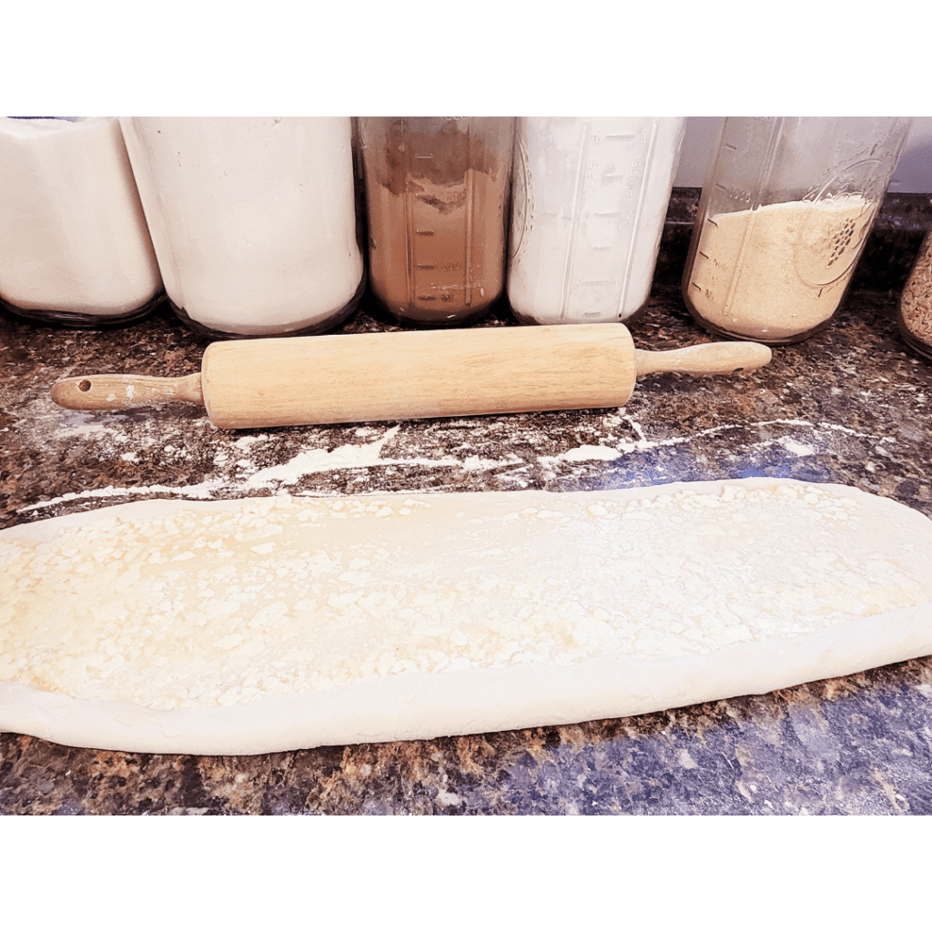 Image illustrates sourdough being rolled out for lemon sugar rolls. 