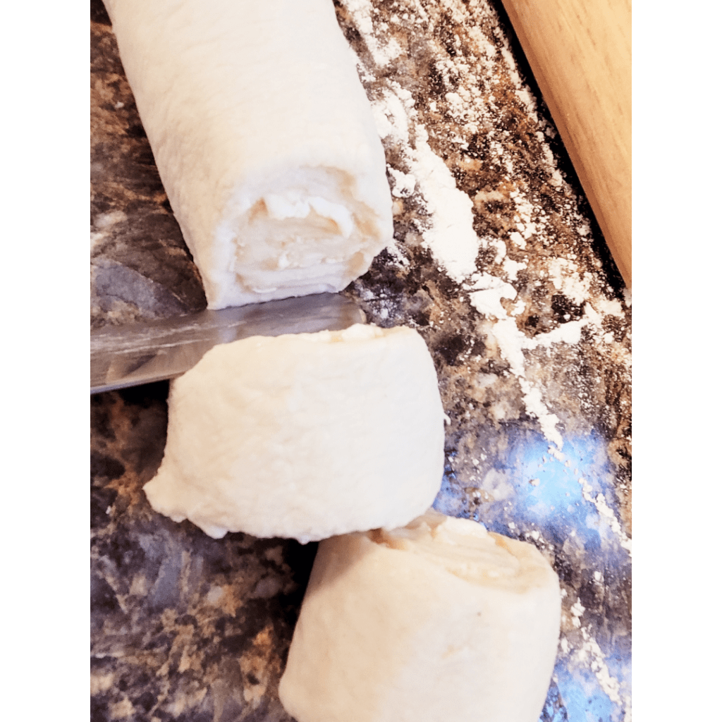 Image illustrates sourdough being sliced out for lemon sugar rolls. 
