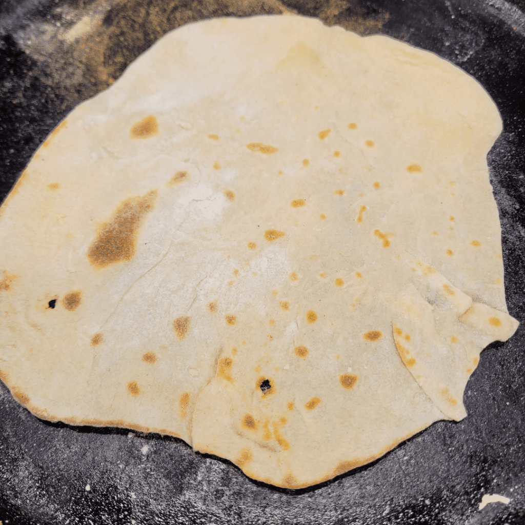 Image illustrates sourdough tortillas cooking on a cast iron skillet.