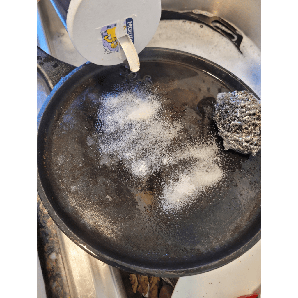 Image illustrates a cast iron pan being cleaned with a salt scrub demonstrating how to season cast iron for cooking. 