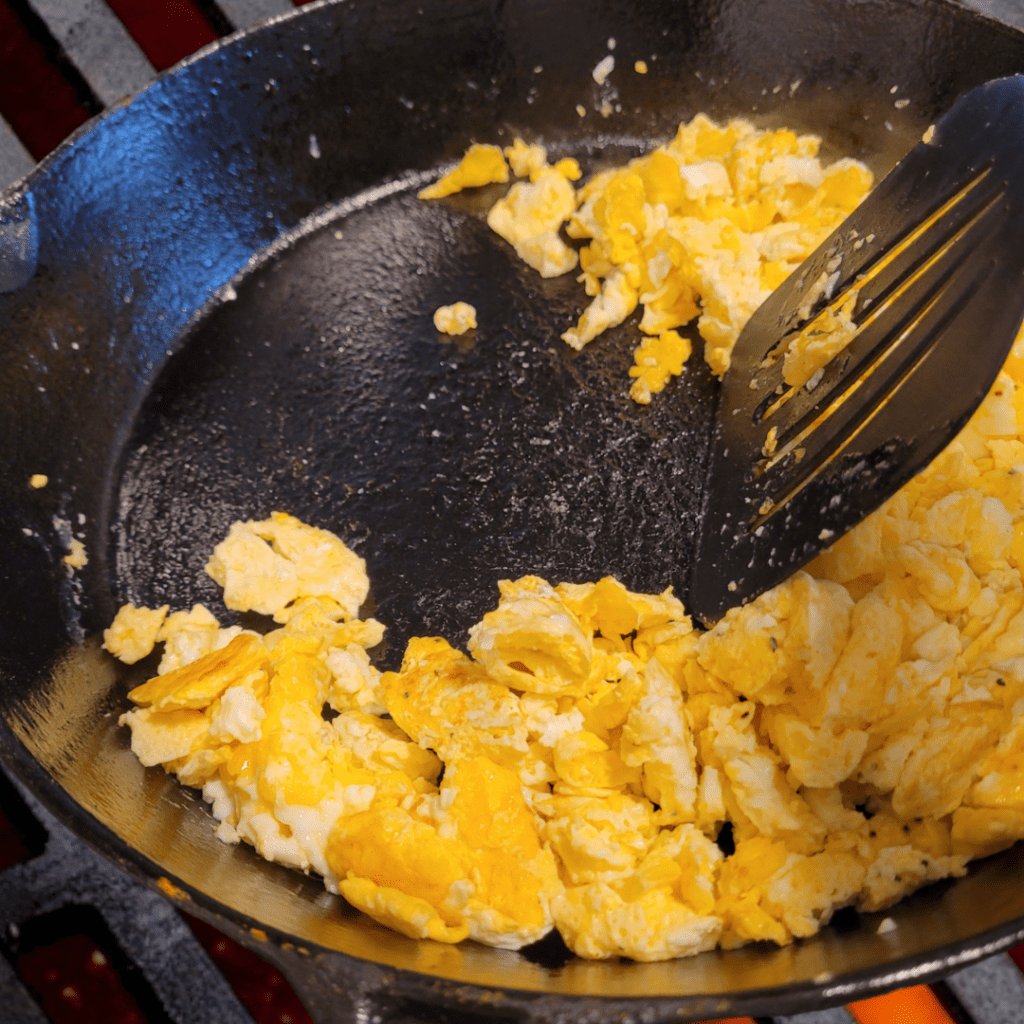 Image illustrates scrambled eggs in a cast iron skillet.