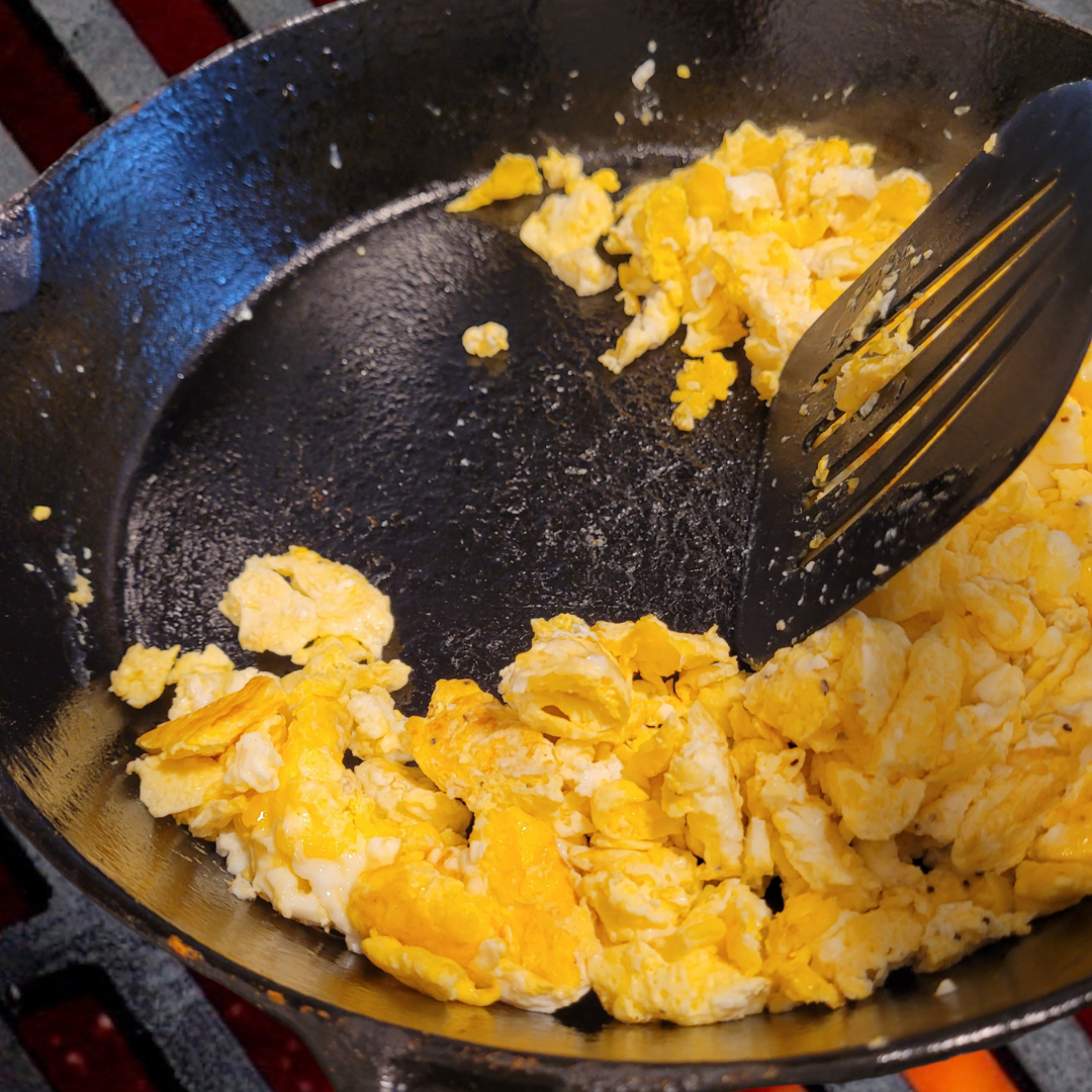 Image illustrates scrambled eggs in a cast iron skillet.