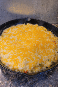 Image illustrates cheese potato casserole in a cast-iron skillet.