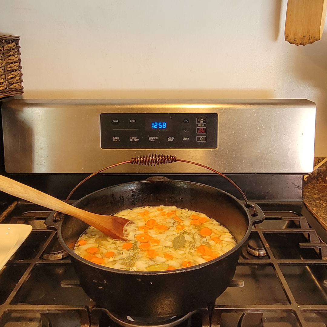 Image illustrates chicken soup in a cast iron pan or cauldron.